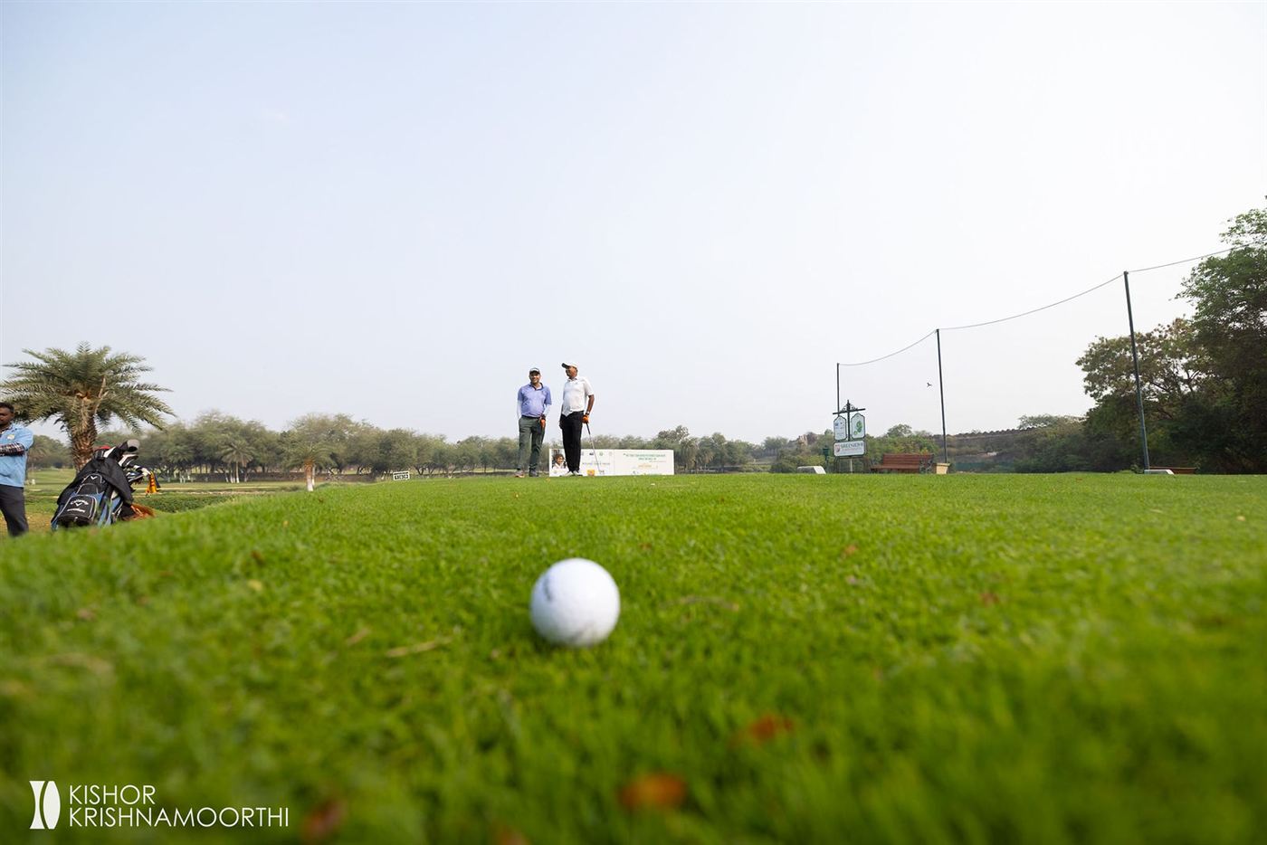 A golf ball on the green with players in the distance